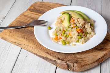 Quinoa porridge with vegetables and avocado in a white flat plate on a wooden board. Superfoods concept and top view.