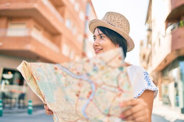 Young latin tourist girl on vacation smiling happy holding map at the city.