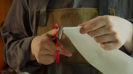 A young master craftsman cuts out patterns from paper with scissors for the author's exclusive...