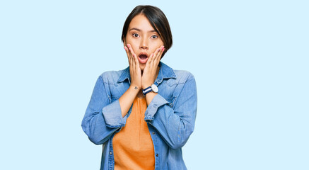 Young beautiful hispanic woman with short hair wearing casual denim jacket afraid and shocked,...