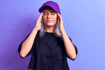 Young beautiful blonde woman wearing t-shirt and purple cap over isolated background with hand on head, headache because stress. Suffering migraine.