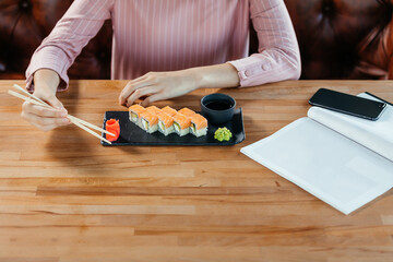 Girl holds wooden sticks in front of a plate of sushi. High quality photo