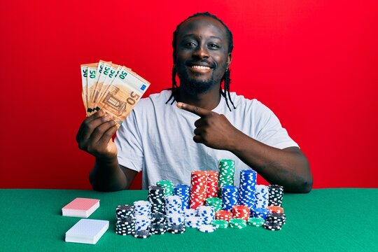 Handsome young black man playing poker holding 50 euros banknotes smiling happy pointing with hand and finger