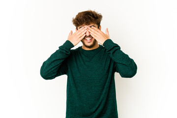 Young arab man on white background covers eyes with hands, smiles broadly waiting for a surprise.