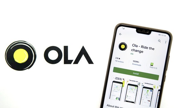 Stone / United Kingdom - February 18 2020: Ola taxi logo projected on the white wall and mobile phone with the Ola app in play market.