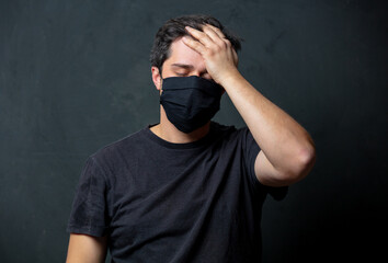 Tired brunet man in in black facemask on dark background