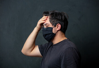 Tired brunet man in in black facemask on dark background