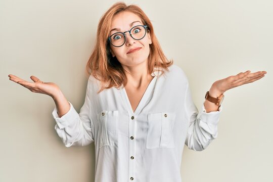 Young caucasian woman wearing casual clothes and glasses clueless and confused with open arms, no idea and doubtful face.