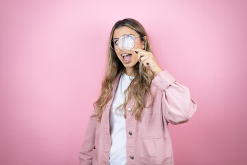 Young beautiful blonde woman with long hair standing over pink background surprised looking through...