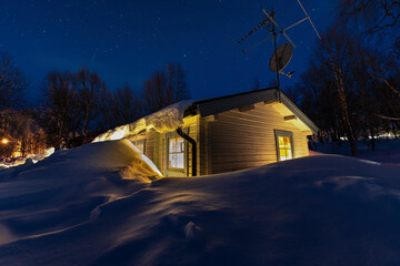 Scenic night photo of typical Swedish wooden mountain cabin with stars above, much snow, birch...
