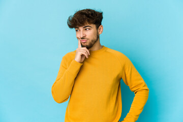 Fototapeta premium Young arab man on blue background contemplating, planning a strategy, thinking about the way of a business.