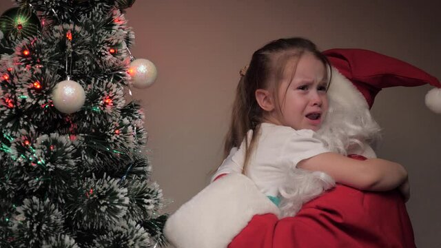 Little girl crying and hugging Santa Claus. The kid is upset Santa Claus calms him down. Happy child's holiday. Winter fairytale visiting kid. Winter holiday new year. Kind magic grandfather