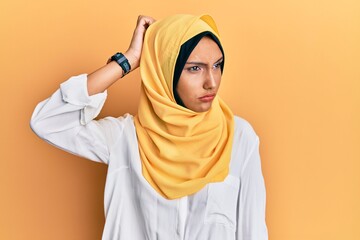Obraz premium Young brunette arab woman wearing traditional islamic hijab scarf confuse and wondering about question. uncertain with doubt, thinking with hand on head. pensive concept.