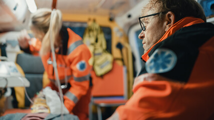 Fototapeta na wymiar Male EMS Paramedics Provide Medical Help to an Injured Patient on the Way to a Healthcare Hospital. Emergency Care Assistants Putting On Non-Invasive Ventilation Mask in an Ambulance. Close-up Shot.