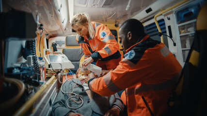 Fototapeta na wymiar Female and Male EMS Paramedics Provide Medical Help to an Injured Patient on the Way to a Healthcare Hospital. Emergency Care Assistants Putting On Non-Invasive Ventilation Mask in an Ambulance.