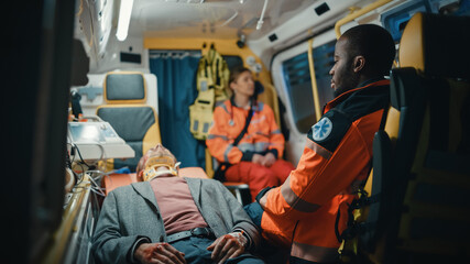 Female and Male EMS Paramedics Ride to Healthcare Hospital with an Injured Patient on the Ambulance. Black African American Emergency Care Assistantis Sitting Next Sick Young Man with Neck Collar.
