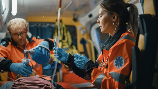 EMS Paramedics Team Provide Medical Help to Injured Patient on the Way to Healthcare Hospital. Female Emergency Care Assistant Injecting a Syringe Shot to Stabilize Vitals of the Man in an Ambulance.