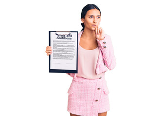 Young beautiful latin girl holding clipboard with terms and conditions document serious face...