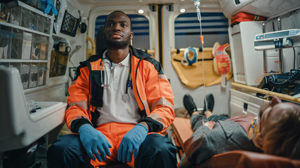 Black African American EMS Professional Paramedic Sit Next to Injured Patient on the Way to Hospital. Emergency Medical Technicians are on Their Way to Healthcare Hospital with Patient. © Gorodenkoff