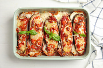 Baked eggplant with tomatoes, cheese and basil in dishware on white wooden table, flat lay