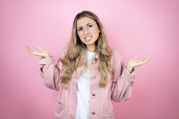 Young beautiful blonde woman with long hair standing over pink background clueless and confused...