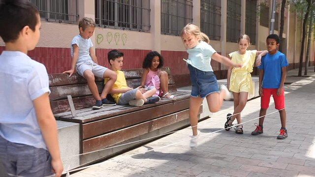Happy little girl jumping game by rubber band with friends on the street. High quality FullHD footage