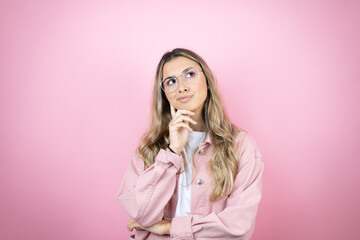 Young beautiful blonde woman with long hair standing over pink background with serious face thinking about question, very confused idea