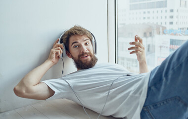 bearded man lying on the windowsill wearing headphones music