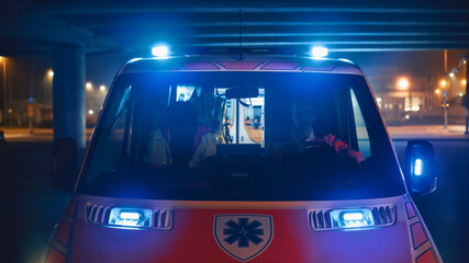 Ambulance Vehicle with Working Strobe Lights and Signal Arrived on the Scene of a Traffic Accident on a Street at Night. Front of the Emergency Paramedics Rescue Van with Medical Cross Logo.