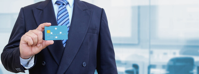 Cropped image of businessman holding plastic credit card with printed flag of Micronesia. Background blurred.
