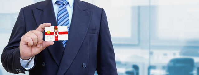 Cropped image of businessman holding plastic credit card with printed flag of Northern Ireland. Background blurred.