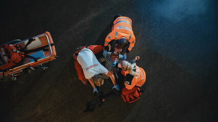 Aerial Portrait of a Young Injured Man Involved in Traffic Accident is Being Saved by Medical Team...