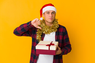 Young caucasian man with christmas hat holding a present isolated on yellow background