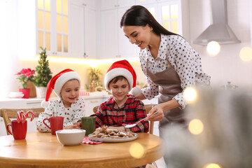 Mother putting sugar powder onto Christmas cookies for her cute little children in kitchen