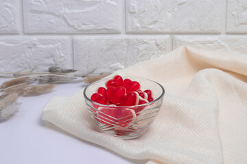 Gelatin hearts in a glass transparent saucer and dried flowers with hare tails on a white background and a brick wall. Valentine's day banner.
