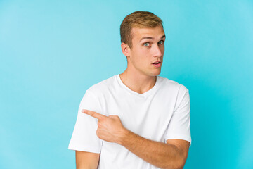 Young caucasian handsome man smiling and pointing aside, showing something at blank space.