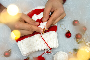 Fototapeta na wymiar men's hands knit New Year's striped red and white hat, cap on gray background of Christmas balls and bokeh