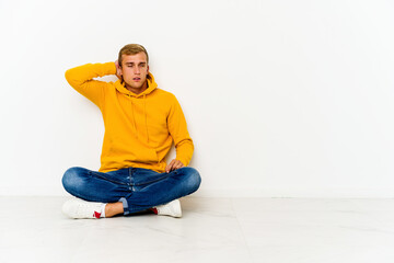 Young caucasian man sitting on the floor tired and very sleepy keeping hand on head.