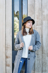 Portrait young pretty Caucasian girl, dressed in a gray jacket, a white sweater and a hat.