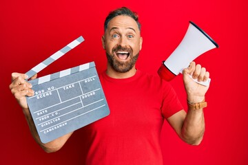 Handsome middle age man holding video film clapboard and megaphone celebrating crazy and amazed for...