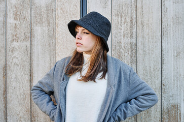 Portrait young pretty Caucasian girl, dressed in a gray jacket, a white sweater and a hat.
