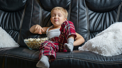 boy on black sofa watching tv and eating popcorn