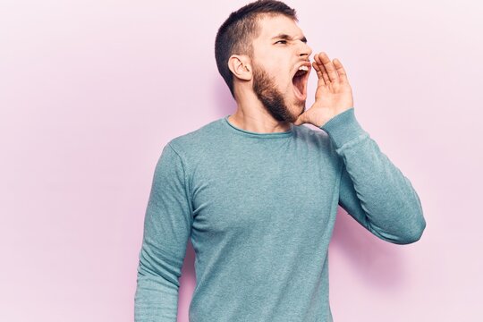 Young handsome man wearing casual sweater shouting and screaming loud to side with hand on mouth. communication concept.
