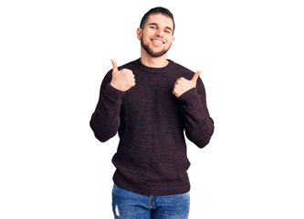 Young handsome man wearing casual sweater success sign doing positive gesture with hand, thumbs up smiling and happy. cheerful expression and winner gesture.