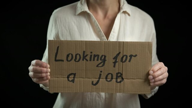 Workless protest. A stressed woman looking for a job with a cardboard on the black background.