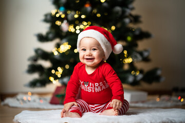 adorable little baby boy in a red christmas outfit sitting on a soft fake fur in front of a christmas tree