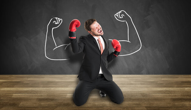 businessman with boxing gloves and powerful pose cheering in front of a blackboard