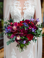 Wedding bouquet of red flowers in the hands of the bride in a white dress