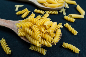 Different types of Italian pasta in spoon on the black background