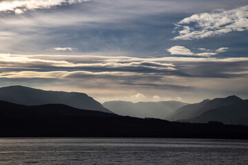 View of Snowdonia mountain range, across the Menai Straits, from Beaumaris. Mountains silhouetted against the late afternoon winter sky, with blue sky, a hint of sunset orange and white fluffy clouds.